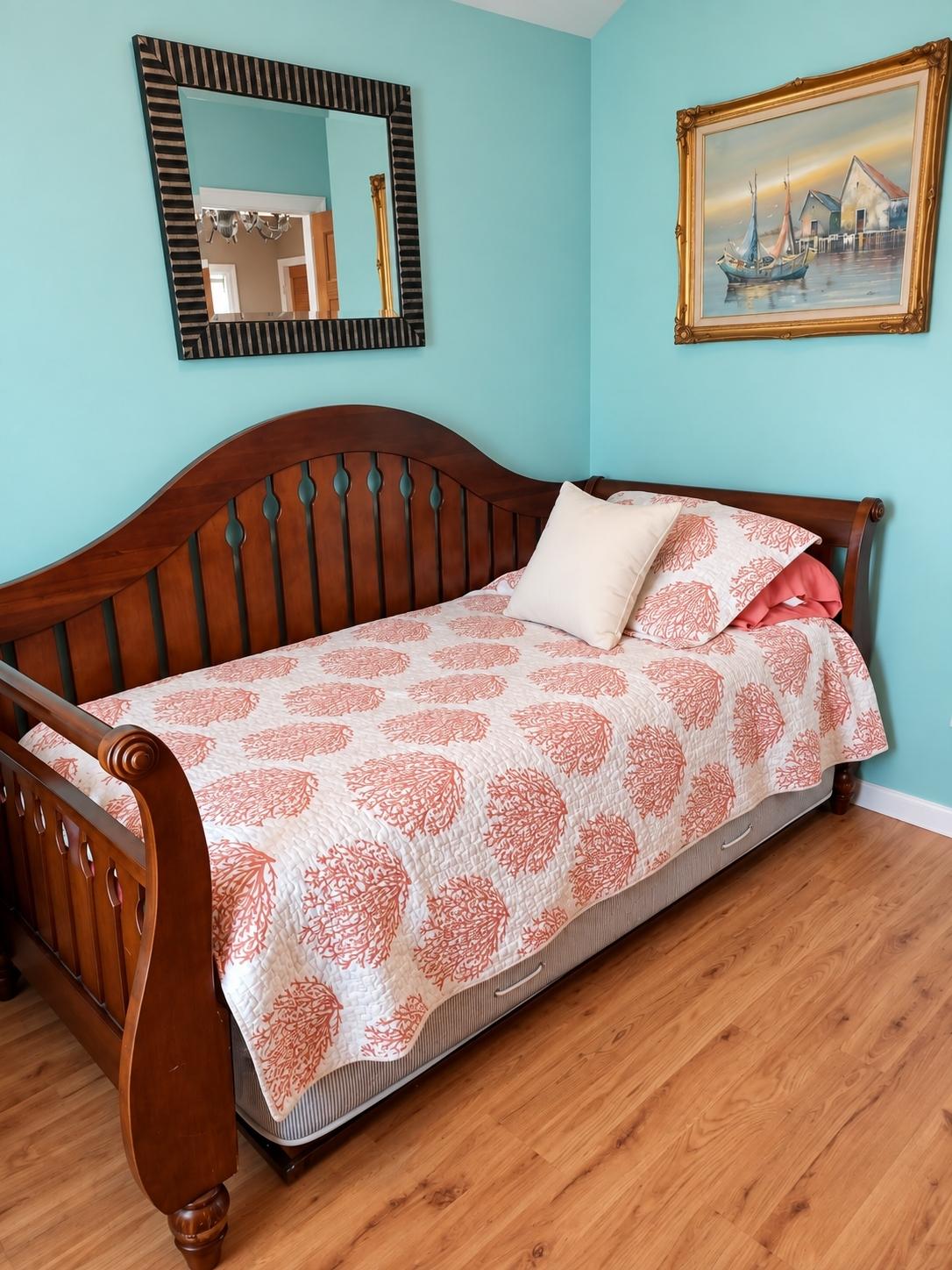 Daybed with coral coastal quilt beneath a gold-framed painting